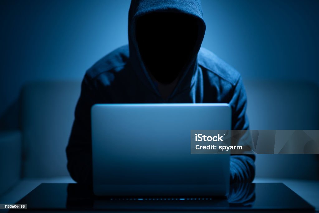 Hacker dark face using laptop Hacker dark face using laptop in the dark room Computer Hacker Stock Photo