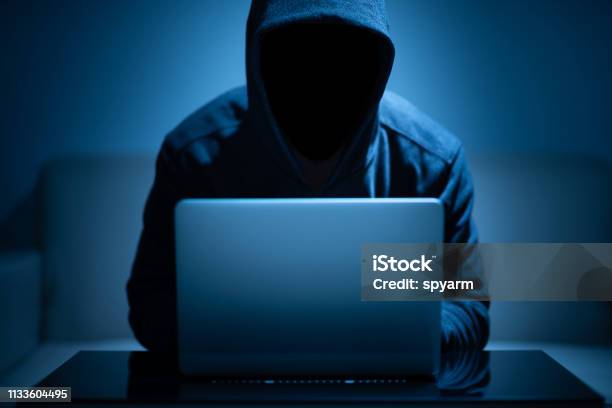 Hacker Dark Face Using Laptop Stock Photo - Download Image Now - Computer Hacker, Computer Crime, Thief
