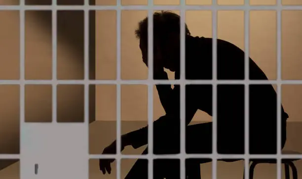 prisoner in prison, silhouette beyond the bars of the cell