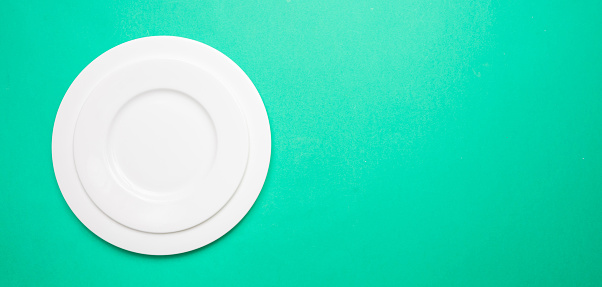Set of empty white plates on green color background, banner, top view, copy space