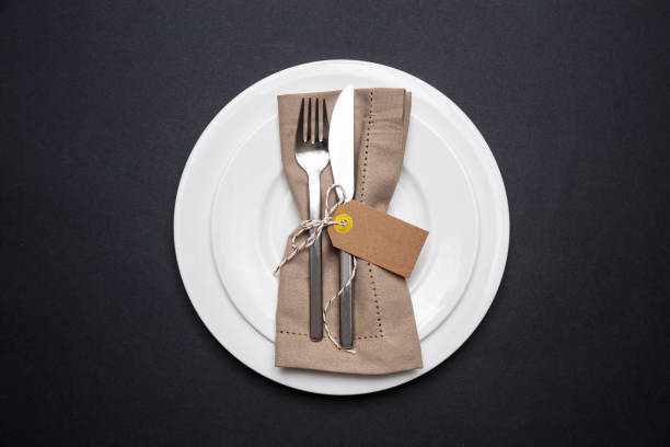 table place setting with linen napkin and blank tag on black color background - silverware fork place setting napkin imagens e fotografias de stock