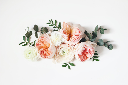 Floral arrangement, web banner with pink English roses, ranunculus, carnation flowers and green leaves on white table background. Flat lay, top view, wedding or birthday styled stock photography.