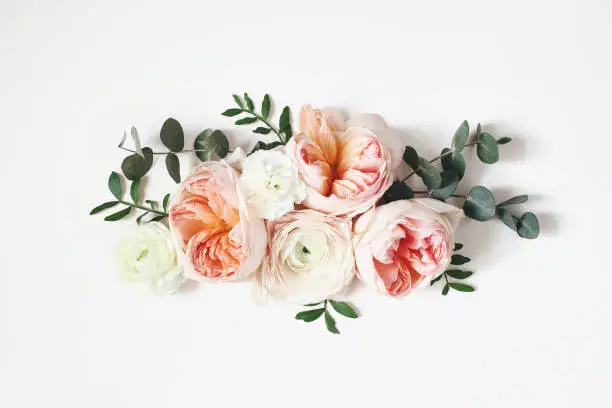 Photo of Floral arrangement, web banner with pink English roses, ranunculus, carnation flowers and green leaves on white table background. Flat lay, top view. Wedding or birthday styled stock photography.