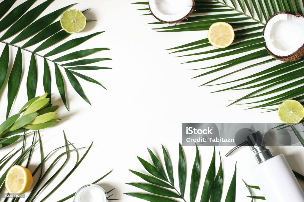 Cadre de beauté de style, bannière Web. Crème pour la peau, bouteille de savon, noix de coco, citrons et fruits à la chaux sur des feuilles de palmier luxuriante. Fond de table blanc. Cosmétique, Spa et concept d'été tropical. Flat Lay, vue de dessu - Photo de Fond libre de droits