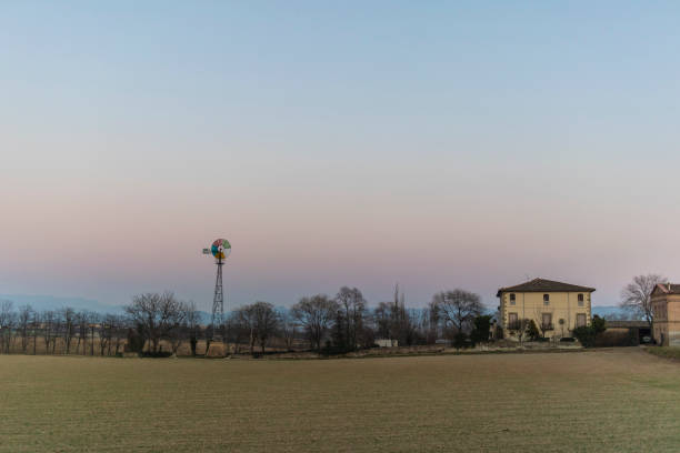Wind mill and farmhouse on a rural sunset landscape  over a plain field