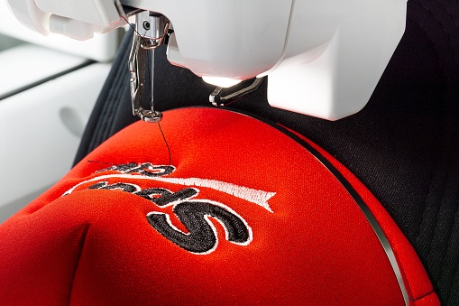 Close up image of embroidered red and black sport cap on the hoop of embroidery machine