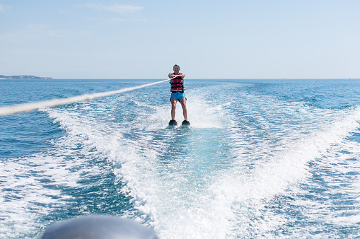 Young man glides on water skiing on the waves on the sea, ocean. Healthy lifestyle. Positive human emotions, joy. Family are spending time at tropical ocean in the day time.