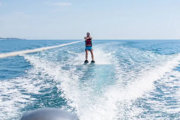 Photo of Young man glides on water skiing on the waves on the sea, ocean. Healthy lifestyle. Positive human emotions, joy. Family are spending time at tropical ocean in the day time.