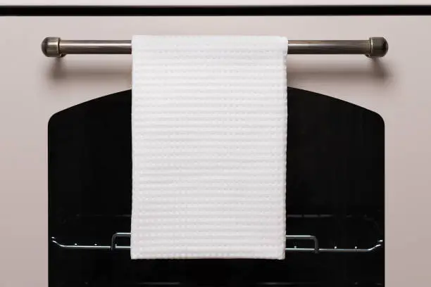 White kitchen towel hangs on the oven handle, product mockup.