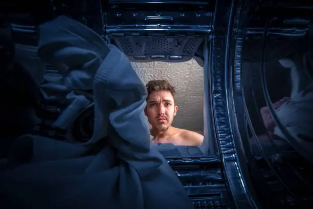 Photo of Young man doing laundry View from the inside of broken washing machine