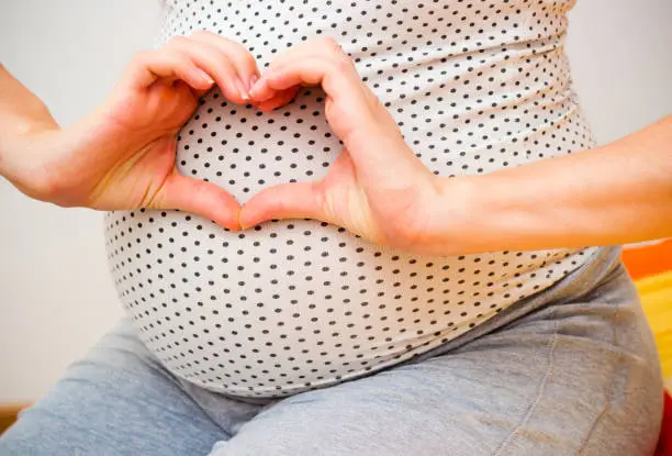 Photo of Happy pregnant woman making heart gesture