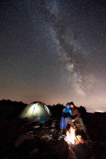 istock Hikers resting at night camp in mountains under starry sky 1133635018