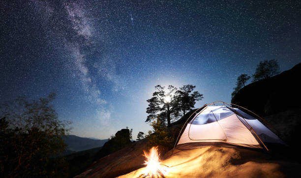Tourist camping on rocky mountain under night starry sky