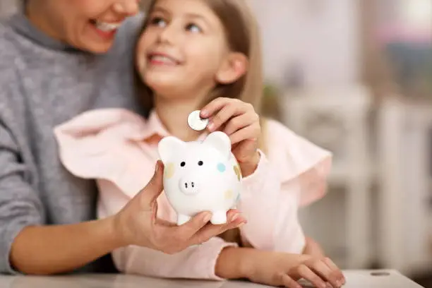 Photo of Young girl and her mother with piggybank sitting at table