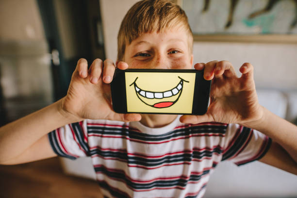 Boy with a smartphone with smiley picture Boy holding a smartphone in front of his face with smiley picture on the display. Boy pretending to be happy at home. mouth photos stock pictures, royalty-free photos & images