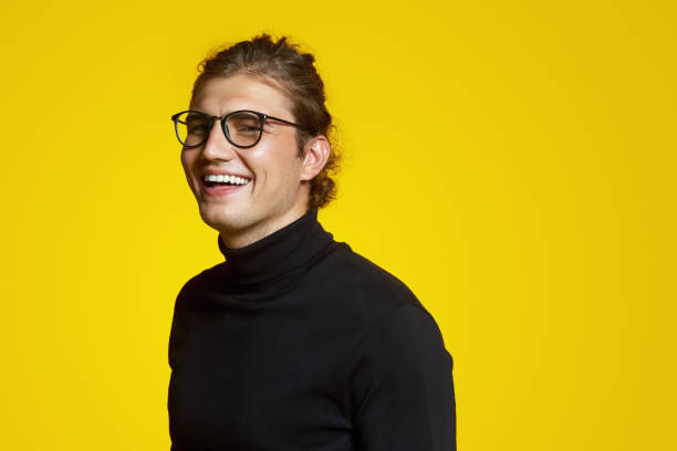 Close up portrait of a cheerful young handsome man in black polo neck and eyeglasses laughing joyful over yellow backdrop Close up portrait of a cheerful young attractive male in black turtleneck and eyeglasses smiling joyful over yellow background high collar stock pictures, royalty-free photos & images