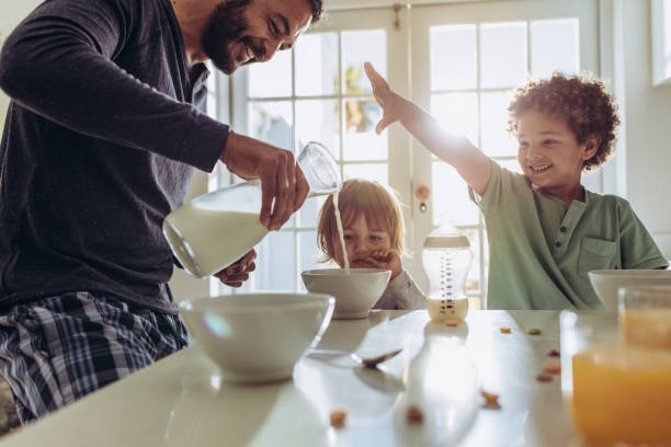 Smiling father pouring milk in to bowls for breakfast Father making breakfast for his kids at home. Man having fun preparing breakfast at home with his kids. breakfast stock pictures, royalty-free photos & images