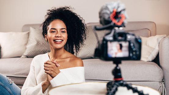Vlogger hembra feliz en vivo de la sala de estar usando la cámara DSLR photo