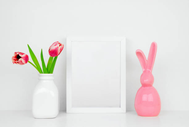 istock Mock up white frame with tulip flowers and modern pink Easter bunny decor on a shelf 1133673706