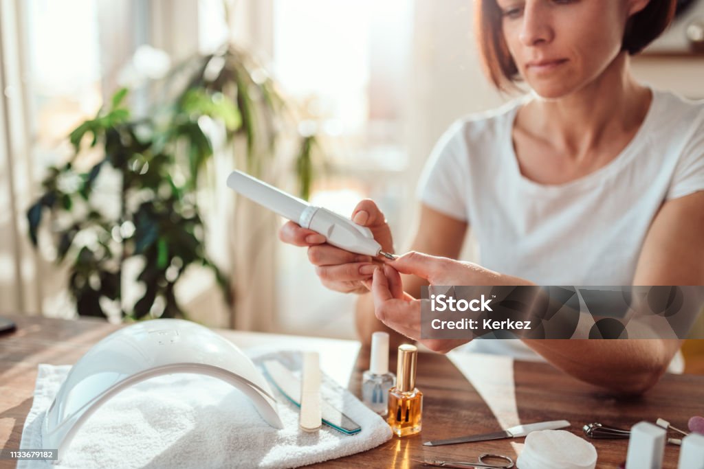 Woman filings nails with electric nail file Woman filings nails with electric nail file at home Fingernail Stock Photo