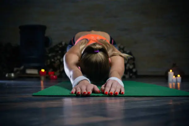 Young enthusiastic woman bending her back on the yoga mat and practicing yoga asana with candles on the background