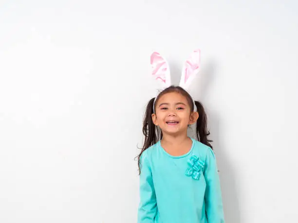 Happy little beautiful girl wearing easter holiday bunny ears on wall white background, Morning sunlight, Concept spring easter day