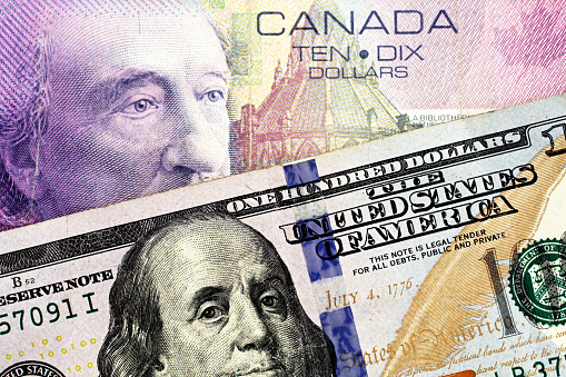A purple Canadian ten dollar bill paired with a blue American one hundred dollar bill