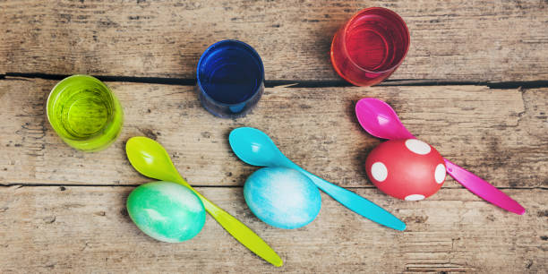 flatlay, colorful easter eggs, egg dyes and spoons on wooden table, header - nodoby imagens e fotografias de stock