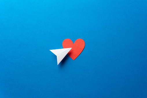 Paper airplane with red heart shape on blue background. Sharing and send symbol concept. Airplane flight transport sign. Landing page concept. Paper plane email web message sending.