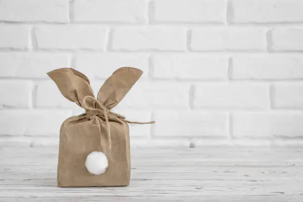 Photo of Decoration Happy Easter background concept. Flat lay minimalism paper bag same bunny or rabbit for gift or present on white brick wall.