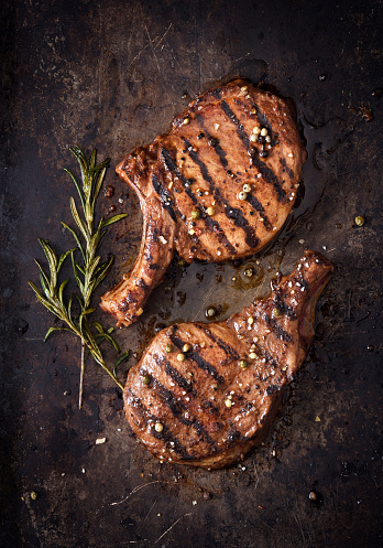 Two juicy grilled pork chops with spices on a dark background
