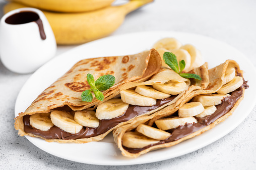 Crepes stuffed with chocolate spread and banana on white plate. Thin pancakes, blini. Sweet dessert.