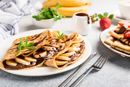 Chocolate hazelnut spread and banana filled crepes on plate. Tasty crepes or blini with sweet sauce and fruits. Closeup view