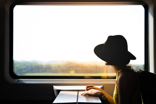 Young pretty woman traveling alone by train looking at the view through the window. A beautiful hipster asian woman traveling on the train. Sitting on the black leather cozy comfort seat in the business class of the train in Europe. Tourist travel concept. self awareness stock pictures, royalty-free photos & images