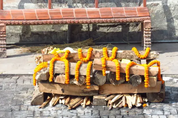 Funeral pyre of wood adorned with marigold flowers for cremation of a dead loved one near the Bagmati River at the Hindu Pashupatinath Temple, Kathmandu, Nepal