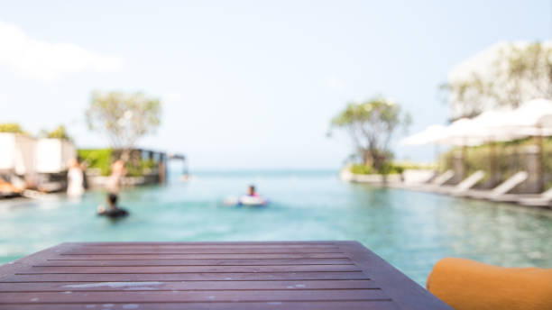 Empty dark wood table with blur people relaxing and enjoy a luxury infinity swimming pool in the beach hotel. Background usage or present your product\ncan be used as mock up or copy space for product presentation