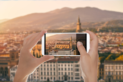 A man is making a photo of panorama of Florence at sunset with the Basilica di Santa Croce (Basilica of the Holy Cross) illuminated by the setting sun on a mobile phone