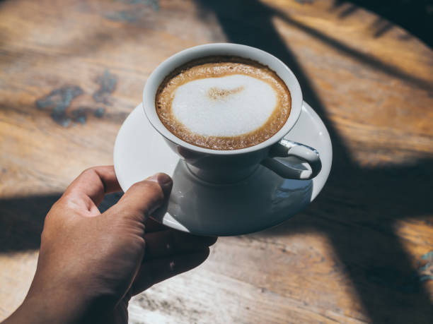 istock Hand holding hot coffee in round white ceramic cup on wooden table background 1133739994
