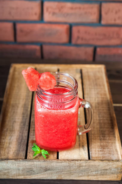 istock Watermelon refreshing smoothie in a jar close-up and copy space. Watermelon smoothie with a heart of watermelon, mint, ice on a textured red brick wall. 1133741278