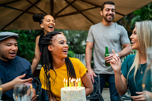 Cheerful friends celebrating birthday party. Men and women are wearing casuals. They are enjoying social gathering in yard.