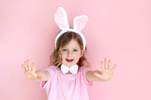 Cute little child wearing bunny ears on Easter day on pink background. Easter girl portrait, funny emotions, surprise. Copyspace for text.