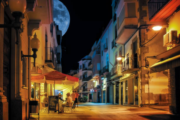 Palamos, Spain - October 5, 2011: A group of residents of the Spanish city of Palamos chatting peacefully near a small street night cafe, against the background of the full moon.