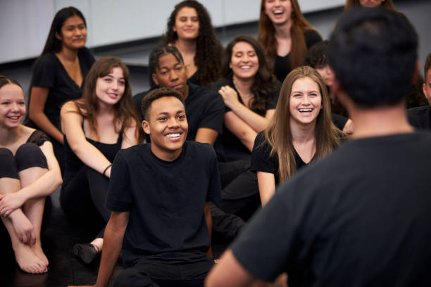 lehrer an der performing arts school talking to students sitting on floor in rehearsal studio - tanzstudio stock-fotos und bilder