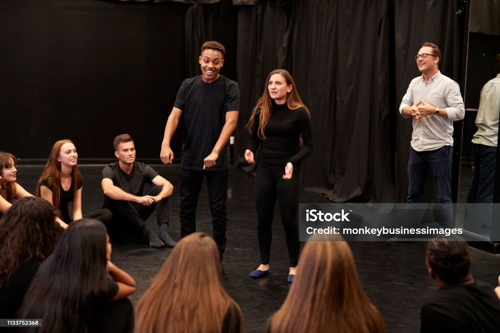 Insegnante con studenti di recitazione maschile e femminile alla Performing Arts School in corso di improvvisazione in studio - Foto stock royalty-free di Spettacolo teatrale