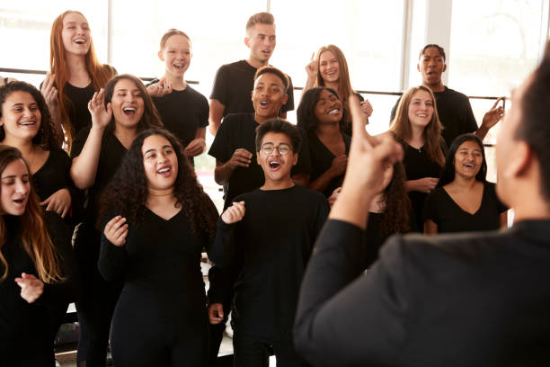männliche und weibliche schüler singen im chor mit lehrer an der performing arts school - music lessons stock-fotos und bilder