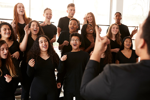 Estudiantes masculinos y femeninos cantando en coro con profesor en la escuela de artes escénicas photo