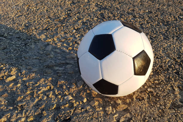 A soccer ball lays on a field where the grass has been cut. Ready for kick off. The ball is seen from the side. Blue sky with some clouds in the background.