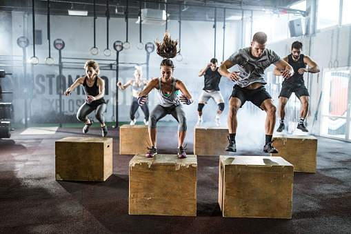 Large group of athletic people exercising jumps on crates during gym training in a gym.