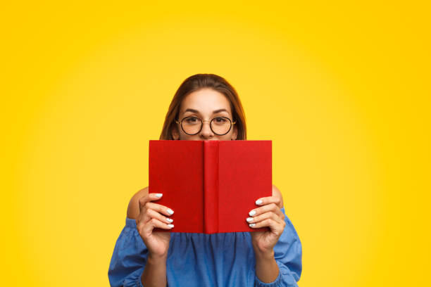 donna con gli occhiali che tiene il libro vicino al viso - tipping over foto e immagini stock