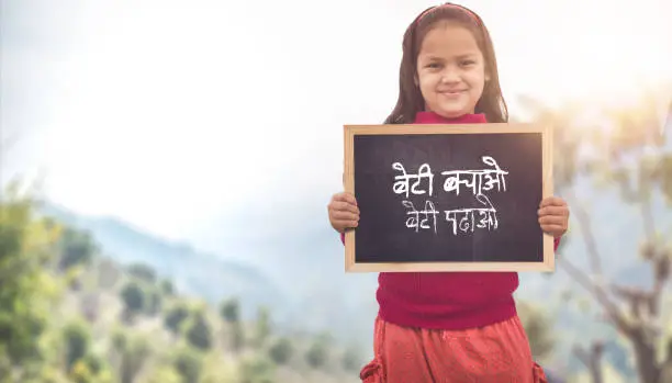 Photo of Adorable little 6-8 years old Indian girl smiling, holding beti bachao beti padhao chalkboard. Save and educate Daughter concept